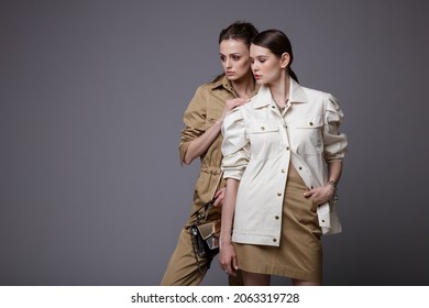 Two high fashion models in white shirt,  beige skirt, jumpsuit, accessories, handbag. Beautiful young women. Studio shot, portrait. Gray background.  Slim figure. Make up, hairstyle - Shutterstock ID 2063319728