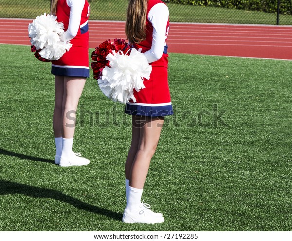 Two high school cheerleaders are standing at\
attention with their pompoms behind them getting ready to start\
their routine.