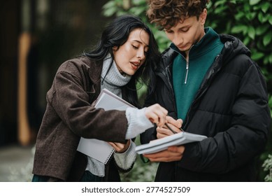 Two high school friends study from notebooks while talking and pointing at notes. A student pair reviews papers outdoors, collaborating on classwork and sharing study tips.