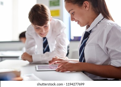 Two High School Students Wearing Uniform Working Together At Desk Using Digital Tablet