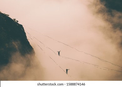 Two highliners are on a line above the cloud. Highliner in the mountains above the canyon. Tightrope walkers over the abyss. A man is walking along a stretched sling. Man catches balance. 