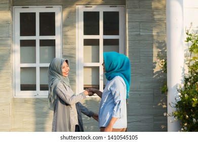 Two Hijab Women Neighbors Meet And Say Hi While Smiling And Shake Hands In Front Of Their House On A Sunny Day