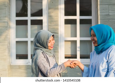 Two Hijab Women Neighbors Meet And Say Hi While Smiling And Shake Hands In Front Of Their House On A Sunny Day