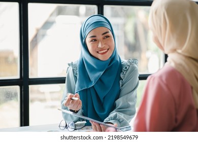 Two hijab-clad Asian women are brainstorming together in a conference room for a startup, run by a young, talented woman. The management concept runs the company of female leaders to grow the company. - Powered by Shutterstock