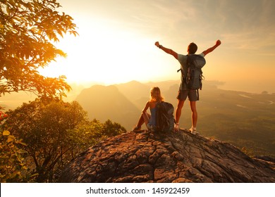 Two Hikers Enjoying Sunrise From Top Of A Mountain