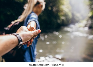 Two hikers in nature. Closeup of man and woman holding hands while crossing the creek. Focus  on hands of couple.
