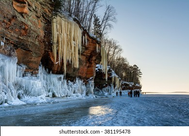 Two hikers provide scale as a sunset accentuates the amber color of the icicles hanging from the sandstone cliffs on Wisconsin's Apostle Islands National Lakeshore near Meyer's beach; Lake Superior.