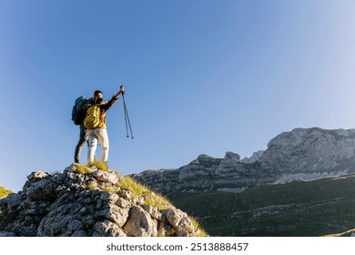 Two hikers stand triumphantly on a mountain peak, raising their trekking poles under a clear blue sky. - Powered by Shutterstock