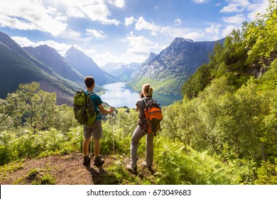 Two hikers at viewpoint in the mountains enjoying beautiful view of the valley with a lake and sunny warm weather in summer, green trees around