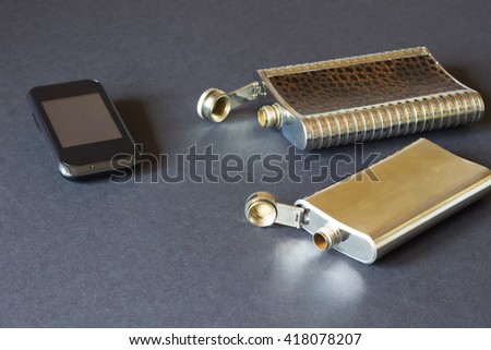 Two hip flasks and cellphone on a black background