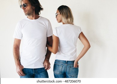 Two hipster models man and woman wearing blanc t-shirt, jeans and sunglasses posing against white wall, toned photo, front and back tshirt mockup for couple