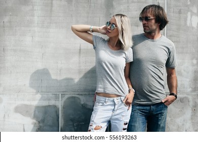 Two Hipster Models Man And Woman Wearing Blank Gray T-shirt, Jeans And Sunglasses Posing Against Rough Concrete Wall In The City Street, Front Tshirt Mockup For Couple, Urban Style