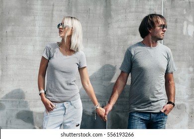 Two Hipster Models Man And Woman Wearing Blank Gray T-shirt, Jeans And Sunglasses Posing Against Rough Concrete Wall In The City Street, Front Tshirt Mockup For Couple, Urban Style