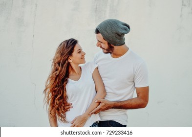 Two Hipster Models Man And Woman Wearing Blanc T-shirt, Jeans And Sunglasses Posing Against White Wall, Toned Photo, Front Tshirt Mockup For Couple