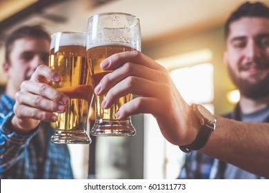 Two hipsters clinking glasses of beer at bar. Cheers. - Powered by Shutterstock