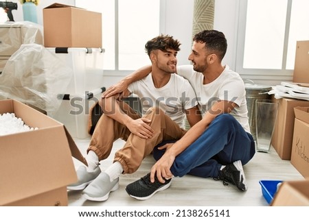 Two hispanic men couple smiling confident hugging each other sitting at new home