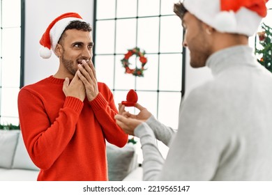 Two Hispanic Men Couple Surprise With Engagement Ring Standing By Christmas Decor At Home