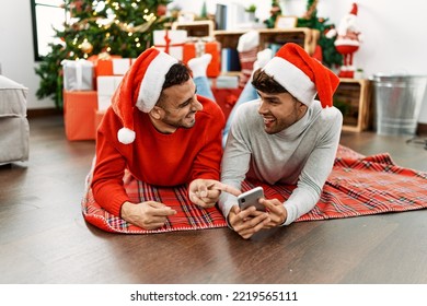 Two hispanic men couple using smartphone lying by christmas tree at home - Powered by Shutterstock