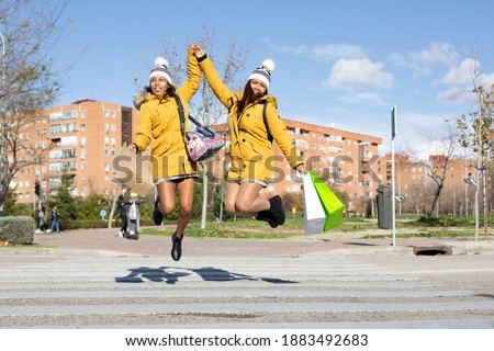 Two hispanic women jumping in the middle of the street with their shopping bags. Space for text.