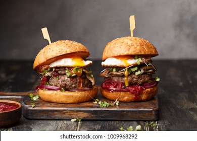 Two homemade beef burgers with mushrooms, micro greens, red onion, fried eggs and beet sauce on wooden cutting board. Side view, close up - Powered by Shutterstock