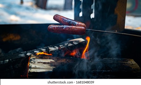 Two hot dogs on a stick roasting on a camp fire on a winter evening  - Powered by Shutterstock