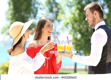 Two hotel customers on summer vacations and a waiter serving them drinks with the ocean in the background - Powered by Shutterstock