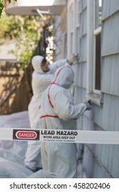 Two house painters in hazmat suits removing lead paint from an old house.