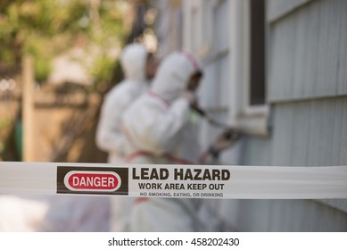 Two house painters in hazmat suits removing lead paint from an old house.