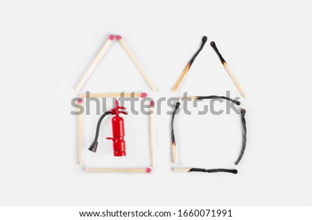 Two houses made of burnt and unburned matches with a miniature fire extinguisher inside the undemaged one. Fire insurance idea