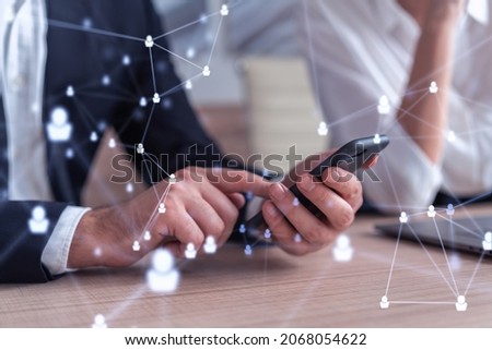Two HR specialists in formal wear analyzing the market using phone to find new interns for recruitment program at international consulting company. Social networking and media hologram icons.