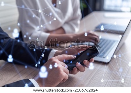 Two HR specialists in formal wear analyzing the market using phone to find new interns for recruitment program at international consulting company. Social networking and media hologram icons.