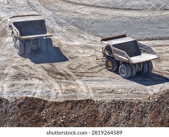 Two huge CAEX class mining haul trucks manoeuvring inside an open pit seen from above