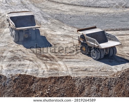 Two huge CAEX class mining haul trucks manoeuvring inside an open pit seen from above