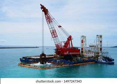 two huge excavators together synchronously on floating platforms in the blue water of the Pacific Ocean extract white sand from the bottom and load onto a barge amid clouds and tropical islands