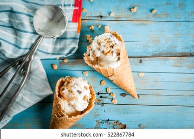 Two ice cream cones with sprinkles of chocolate and cookies on a bright blue wooden table. Summer, bright sun. Top view, copy space 