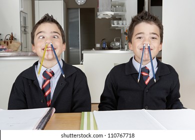 Two identical twin brothers playing with pencils while doing their homework at home on the kitchen table.