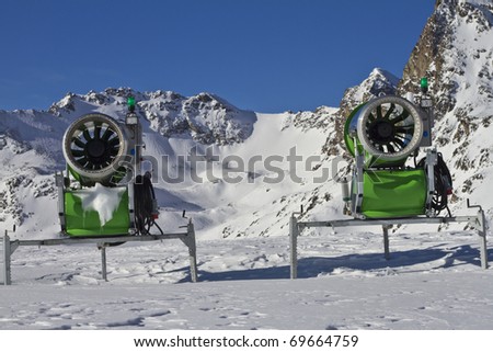 Two idle snowcannons in front of mountains and blue sky