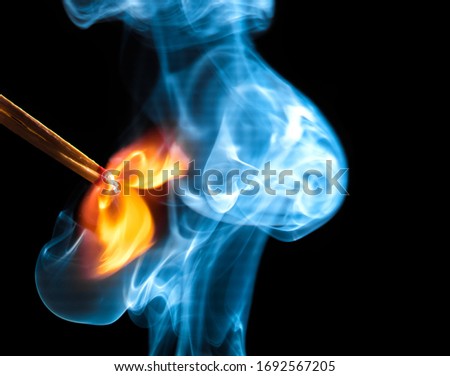 Two igniting matchsticks create a large orange-red flame and bluish smoke against a black background.
