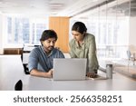 Two Indian business partners meeting at workplace table, talking at laptop, looking at screen, speaking, discussing online startup content, Internet marketing strategy in co-working office