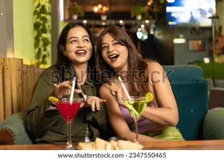 Two indian female friends discussing, laughing and enjoying party together at restaurant.