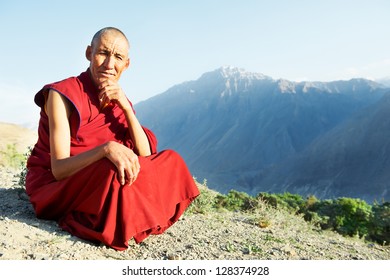 Two Indian tibetan old monks lama in red color clothing sitting in front of mountains