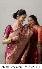 Two Indian women dressed in traditional sarees are adjusting their attire.