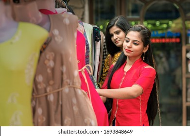 Two Indian Women Shopping Choosing Dresses. Beautiful Young Shoppers In Clothing Store In India.