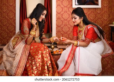Two Indian women wearing traditional saree, gold jewellery and bangles sitting at home with flower and light diyas in decorative background. Indian festival, culture, occasion, religion and fashion. - Shutterstock ID 2061272753