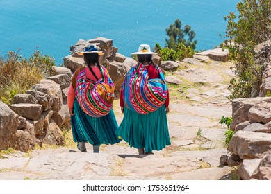 Two indigenous Peruvian Quechua women in traditional clothing walking down the steps to the harbor of Taquile Island, Titicaca Lake, Peru.