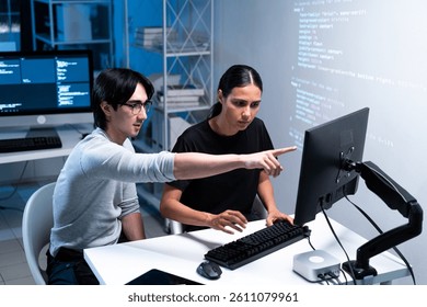Two individuals collaborate at a computer, analyzing code and discussing ideas in a modern workspace.