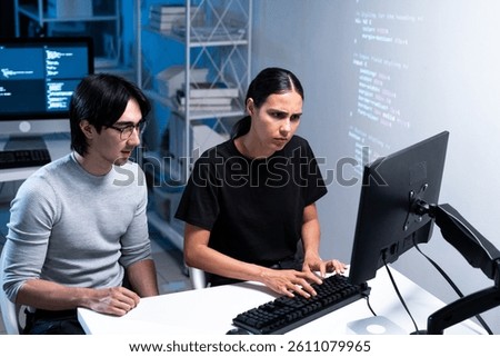 Two individuals collaborate on a computer, focusing intently on coding or programming tasks in a modern workspace.
