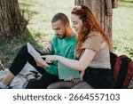 Two individuals sitting under a tree in a park, studying with books and notes, enjoying the outdoors while collaborating and focusing on their work.