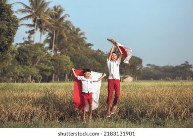 Two Indonesian elementary school student holding flag during independence day in the rice field. Proud primary pupil with Indonesia flag outdoor - Powered by Shutterstock