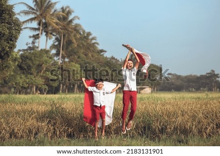 Two Indonesian elementary school student holding flag during independence day in the rice field. Proud primary pupil with Indonesia flag outdoor